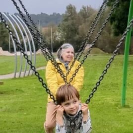 Grandmother in a yellow jacket and young boy enjoying a swing ride together in a green park