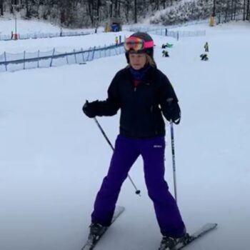 Person skiing on a snowy slope wearing purple pants and a helmet in a winter sports park